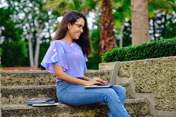 Smiling student girl preparing for exams outdoors with computer