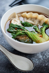 White bowl with dumplings and pak-choi in miso broth, vertical shot, close-up