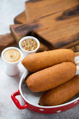 Close-up of corn dogs with mustard, vertical shot on a beige stone surface with wooden chopping boards in the background