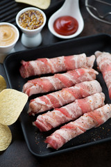 Close-up of a cast-iron pan of raw fresh sausages wrapped with bacon, vertical shot, selective focus