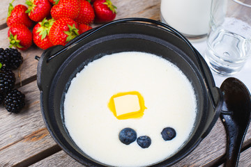 Traditional breakfast milk porridge with butter and berries on a wooden table.