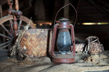 Russian vintage household items. Still life. Old spinning wheel, bast shoes and a kerosene lamp in...