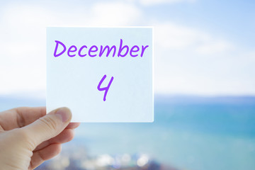 December 4th. Hand holding sticker with text December 4 on the blurred background of the sea and sky. Copy space for text. Month in calendar concept