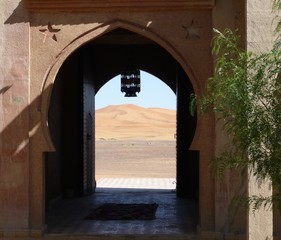 Arched door with tiled entryway,  view of sunlit Sahara sand dunes, hanging lantern -Nomad Palace, Morocco, Inshallah