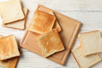 Board with toasts on white wooden background, top view