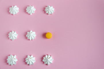 Fototapeta na wymiar Meringue. White airy meringues laid out in rows on a pink background. The rhythmic pattern and one yellow macarone.