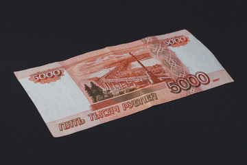 One Russian bill in the amount of 5000 rubles lies on the back on a black background.