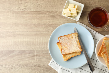 Toasts on plate, towel, tea and butter on wooden background, copy space