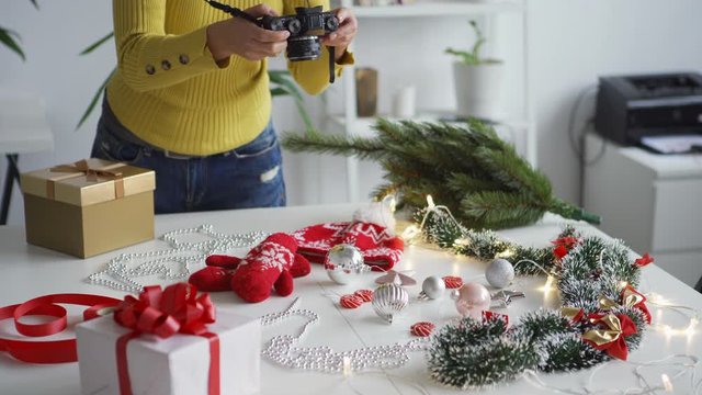 Closeup of unrecognizable female photographer arranging objects on table and taking from above photos of Christmas flatlay with camera
