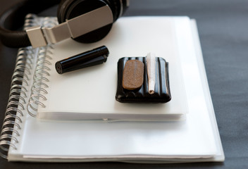 Medical Hashis in the Kingdom of Morocco - CBD medical Moroccan cannabis hashish piece on top of pack of cigarettes, cigar prepared for smoking, books, lighter, headphones, with black background