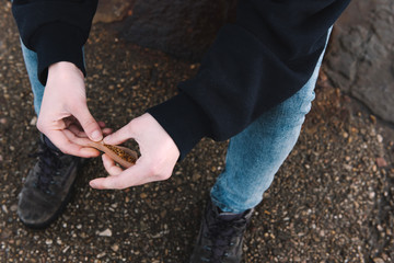 Sailor-like and rough-looking girl with a woolly hat is sitting at the sea port rolling a cigarette. Hands detail. 