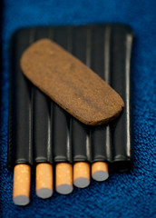 Medical Hashis in the Kingdom of Morocco - CBD medical Moroccan cannabis hashish piece on top of black tobacco pack, 5 cigars, with blue classic background