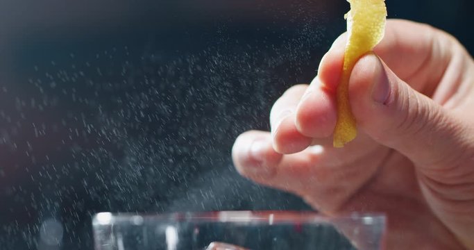 Macro of a professional bartender is squeezing a lemon while preparing an alcoholic cocktail with ice cubes to customers at the bar or disco club.