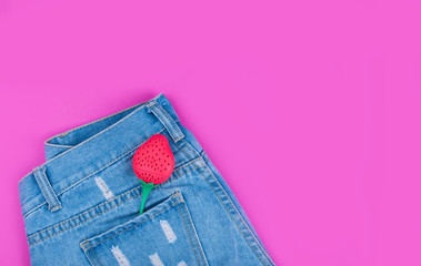 Trendy denim shorts with strawberries in the back pocket against a pink background.