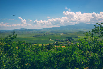 Obraz premium Fantastic summer field in Italy, Tuscany landscape with cloudy sky and fragment of stone wall.View of fields and hills of Tuscany from above the walls