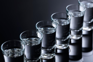 Glasses of vodka on a black reflective background.