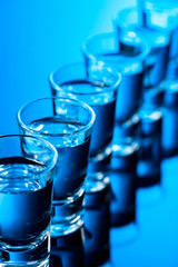 Glasses of vodka on a black reflective background.
