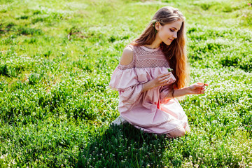 blonde girl in pink dress is collecting flowers in the garden