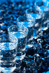Damp glasses of vodka with ice on a black reflective background.