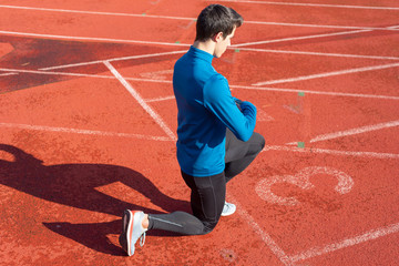 Man athlete on the starting line of a running track at the stadium, resting on his knees .