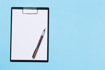 Clipboard with white sheet and pen on a blue background. View from above. space for text