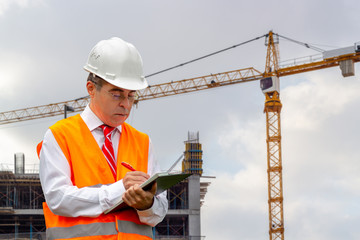 Construction engineer man in shirt and tie with safety helmet and vest works at construction site. Concept of people working in industrial field