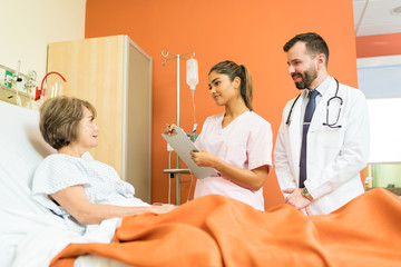 Doctors Communicating With Elderly Patient At Hospital