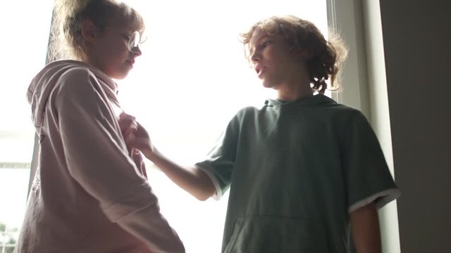 Boy and a girl are standing against each other Indoor in front of the window. Children bully to each other, quarrel, bullying at school