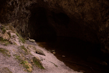 Dark interior of the cave. Abstract natural background with dark zone. Shore of an underground lake. Deep shadow. Mysterious background. Copy space.
