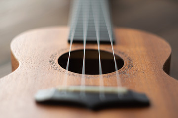 Defocused ukulele strings body, soundhole, bridge and neck on brown wooden background.
