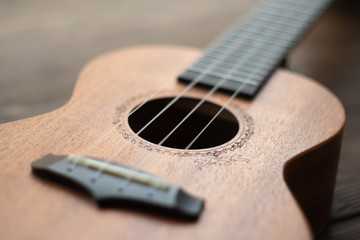 Defocused ukulele body, soundhole, bridge and neck on brown wooden background.