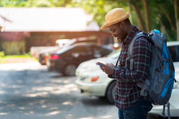 African traveler man using smartphone at car park with holding backpack