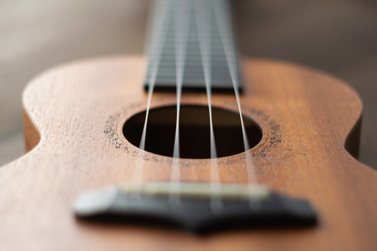 Defocused ukulele strings body, soundhole, bridge and neck on brown wooden background.