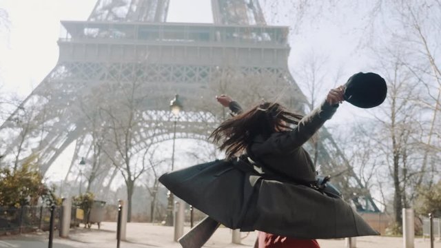 Beautiful happy Caucasian woman spinning cheerfully with open arms at famous Eiffel Tower on Paris vacation slow motion.