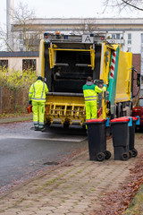 Zwei Müllmänner hinten auf einem Müllfahrzeug auf einer Straße