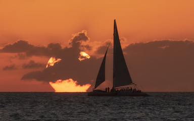 Fototapeta premium a setting sun with a silhouetted sailboat