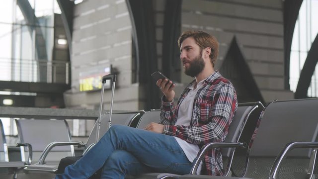Young man using smartphone sitting in waiting hall at train station