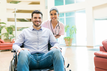 Young Orderly With Recovered Man At Hospital Lobby