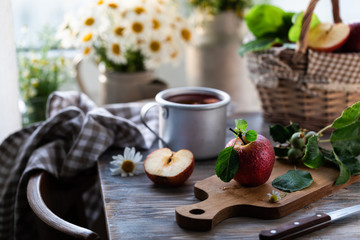 Homemade compote of summer apples on a wooden table by the window. Basket of apples. Wild flowers of the chamomile in the jar