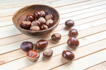 pile of aesculus hippocastanum or conker tree nuts in plate on wooden table