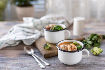 Soup with meatballs in metal mugs on wooden background