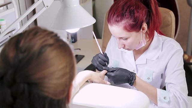 Manicurist woman in cosmetic bath is applying gel on client's nails