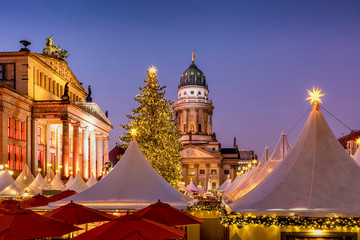 Der Weihnachtsmarkt am Gendarmenmarkt in Berlin am Abend mit den beleuchteten, historischen Gebäuden und festlich geschmücktem Tannenbaum © moofushi