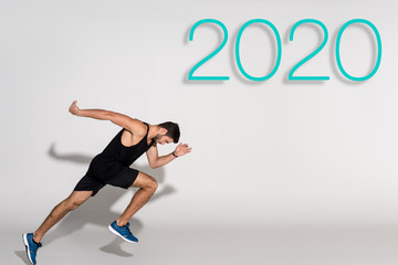 Fototapeta na wymiar side view of sportsman running on white background with 2020 lettering