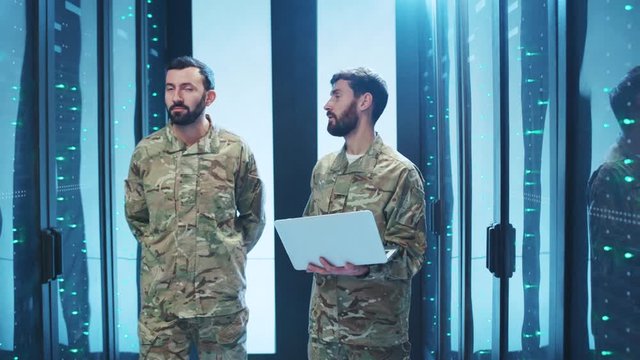 Professional IT military officers in uniform walking with laptop in data center. Two army soldiers inspecting high secure server room at cyber security government facility.