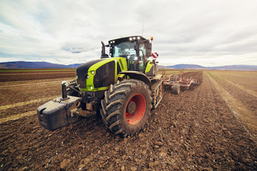 Modern tractor working on the farm, a modern agricultural transport, cultivation of fertile land, tractor on cloudy sky background, agricultural machine. Tractor in full speed