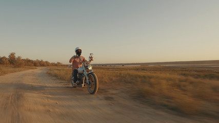Fototapeta na wymiar Motorcyclist driving his motorcycle on the dirt road during sunset