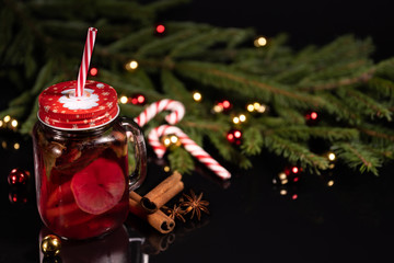 Christmas cocktail with lemon and spices cinnamon and star anise on a black background of a Christmas tree with toys and candy cane