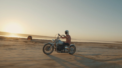 Obraz premium Motocyklista prowadzący motocykl na polnej drodze podczas zachodu słońca