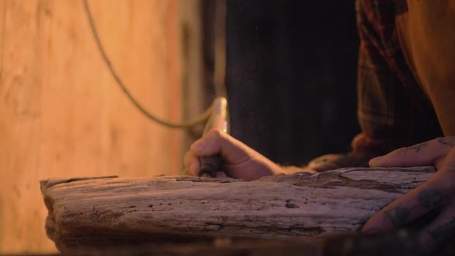 Male using tool equipment holding carving wood art slow motion medium on wooden table in rustic shed from side angle
